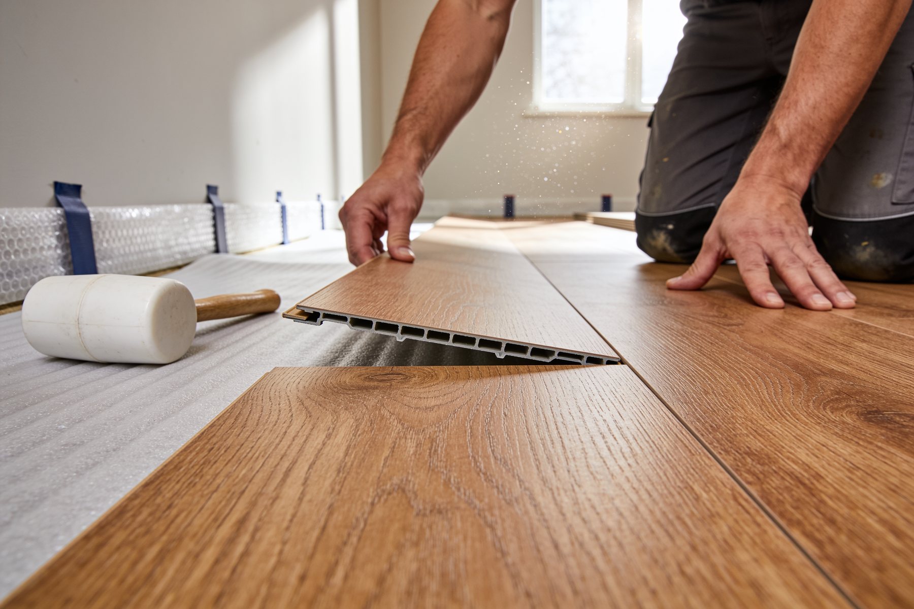 Installer seating a wide plank of oak luxury vinyl flooring into the previous row