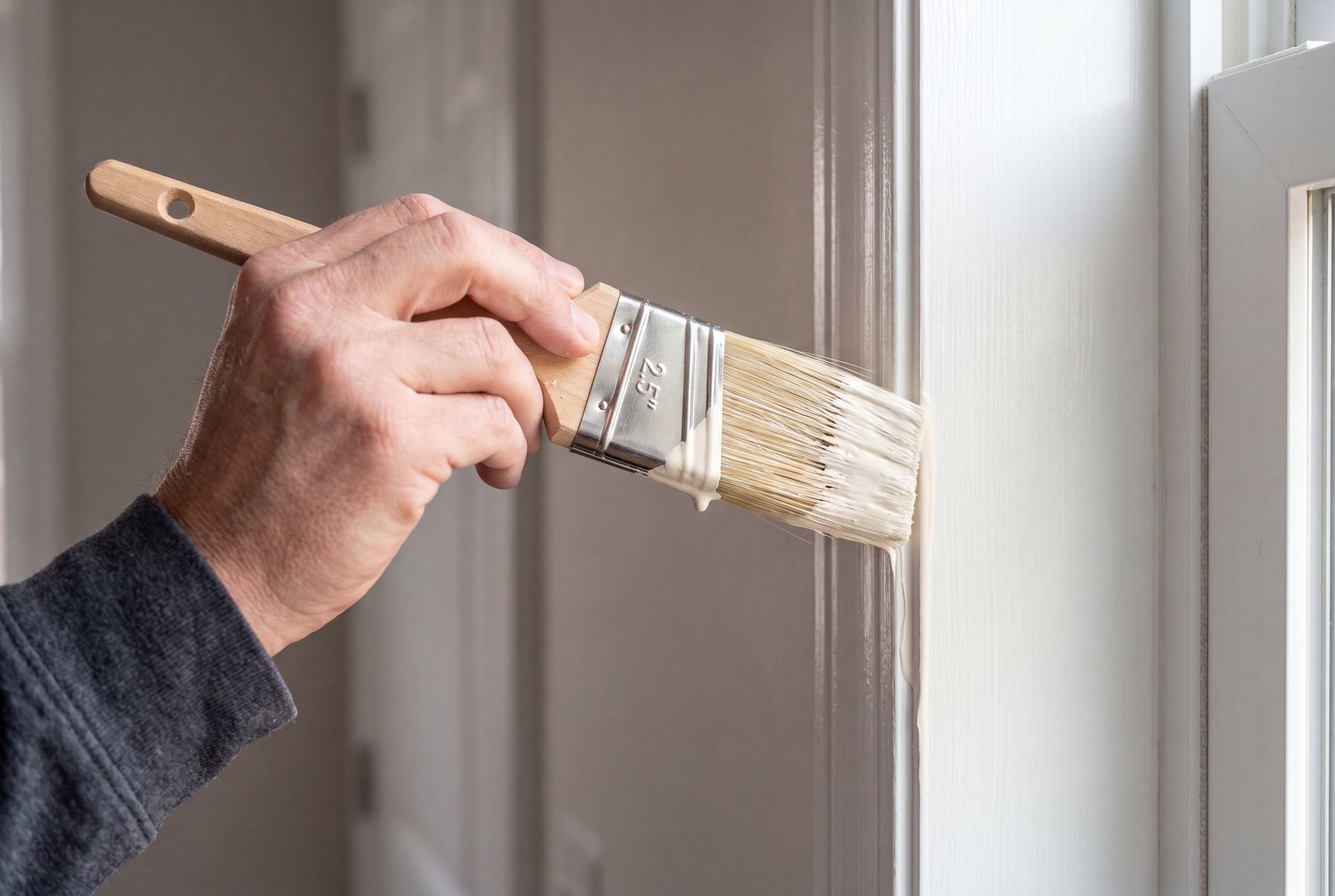 Close-up of a sash brush cutting a sharp paint line against white door trim