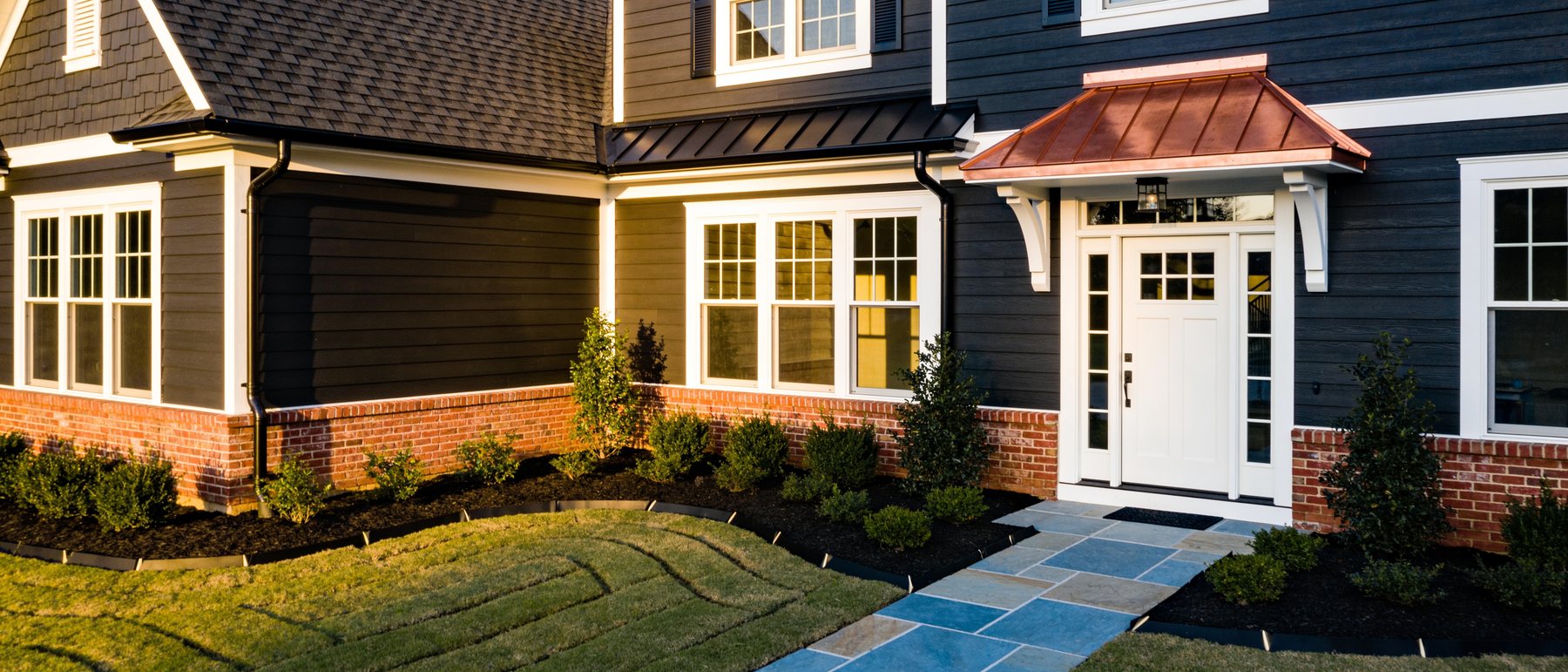 Completed exterior renovation with new siding, roof, front door and freshly installed landscaping