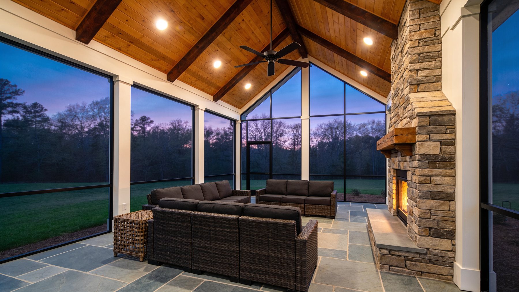 Completed covered porch addition at dusk with cypress ceiling and stone fireplace in Roswell, Georgia