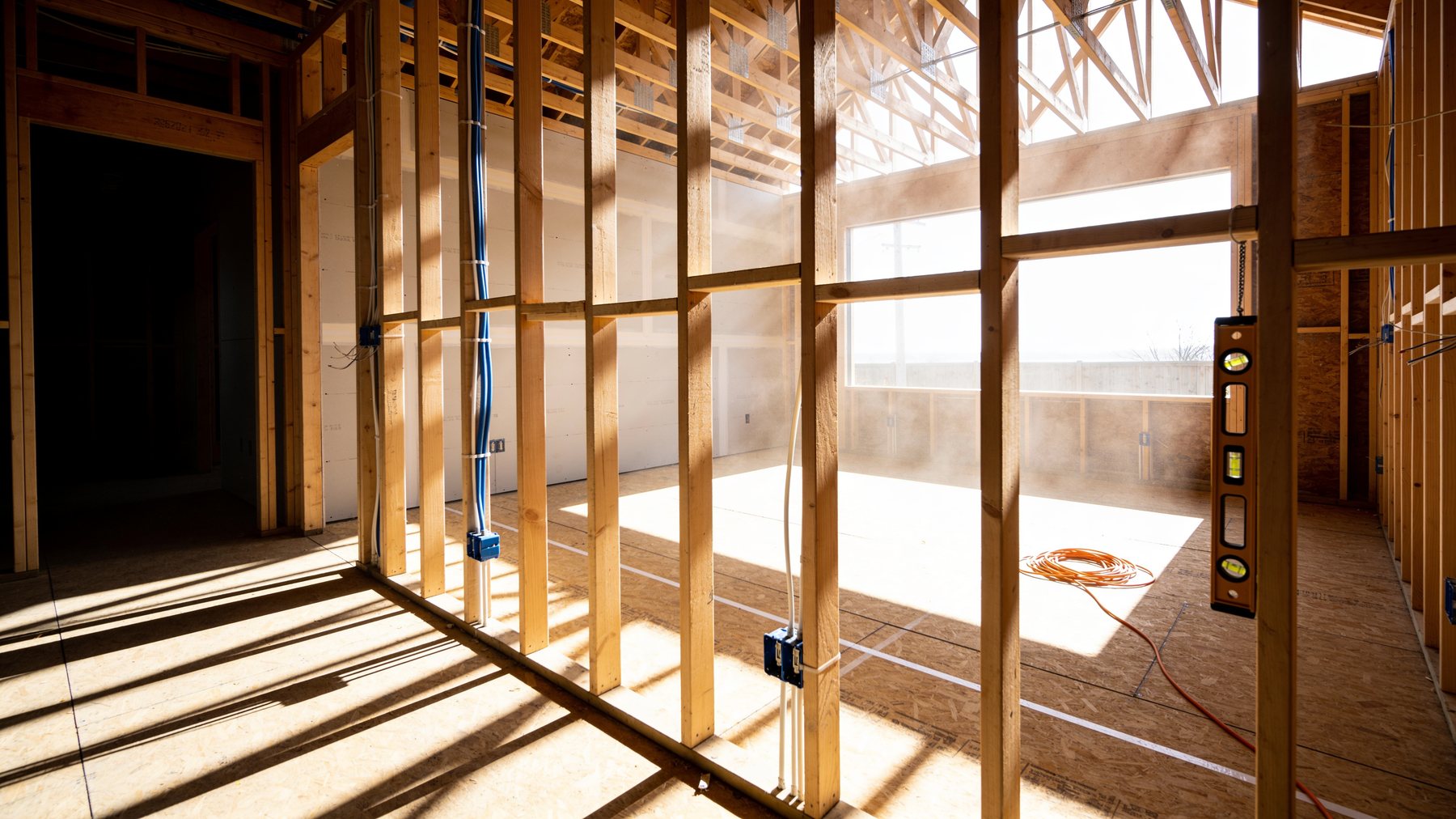 Residential renovation mid-construction: new framing, electrical rough-in and sunbeams through the stud bays