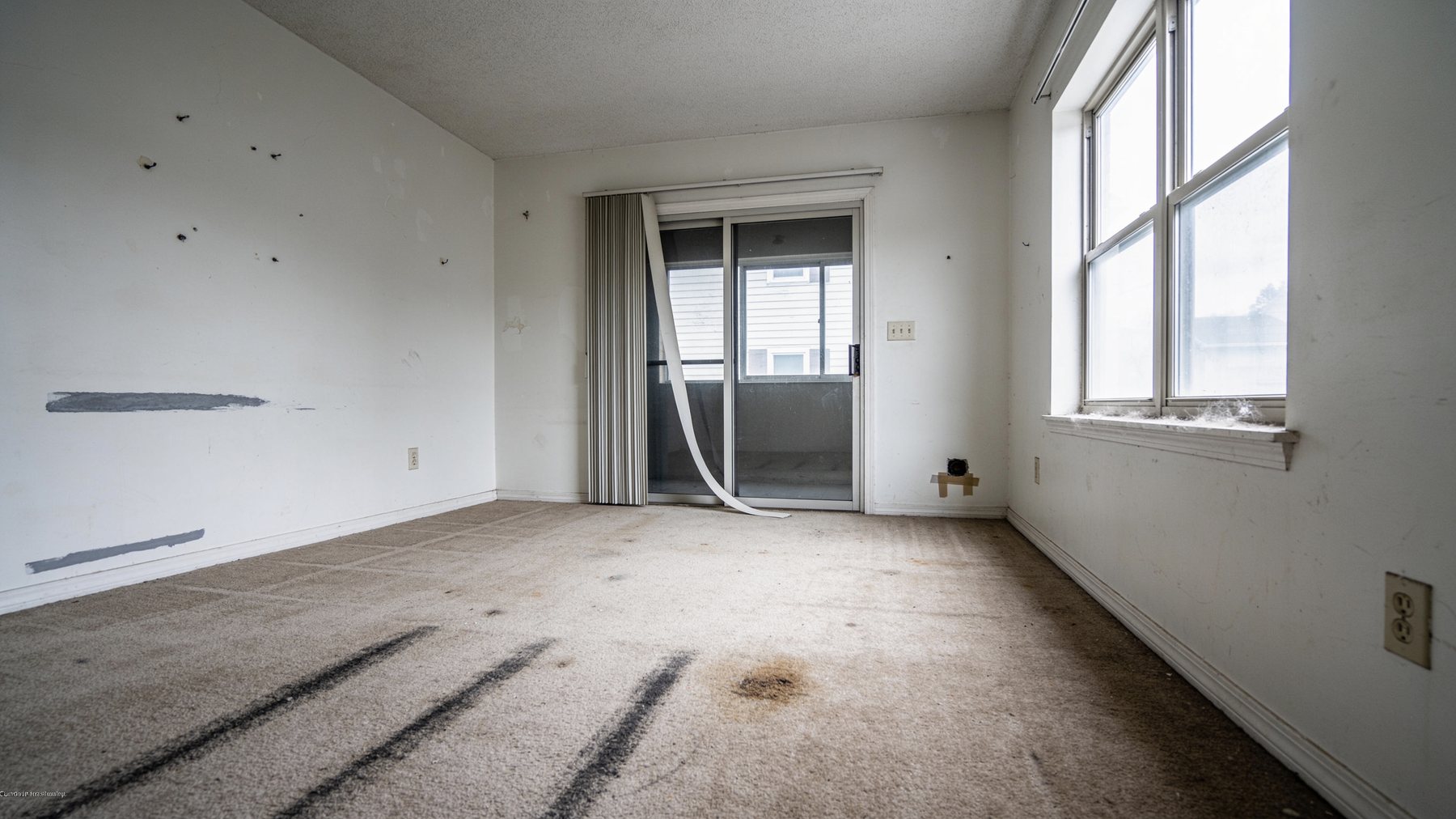 Vacated rental unit before turnover work: scuffed walls, stained carpet and a broken blind
